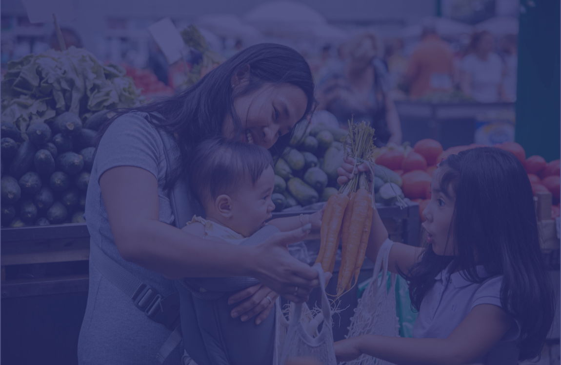 A woman is standing in the store with her 2 children, one son and one daughter. They are smiling and holding the produce while putting it into the cart together.