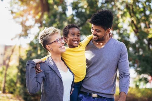 A woman and a man are carrying a child from their shoulders, they are all smiling