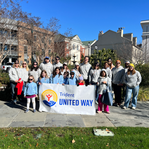 Photo of a group of people posing for the camera. There are children in the front holding a banner with the Trident United Way logo. They are waiting to march in the MLK Day parade in Charleston.