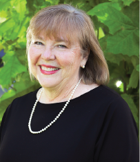 A headshot of Cathy Easley, She is standing in front of a tree and wearing a black top, smiling.
