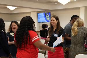 Two women talking, one is smiling at the other and holding a piece of paper