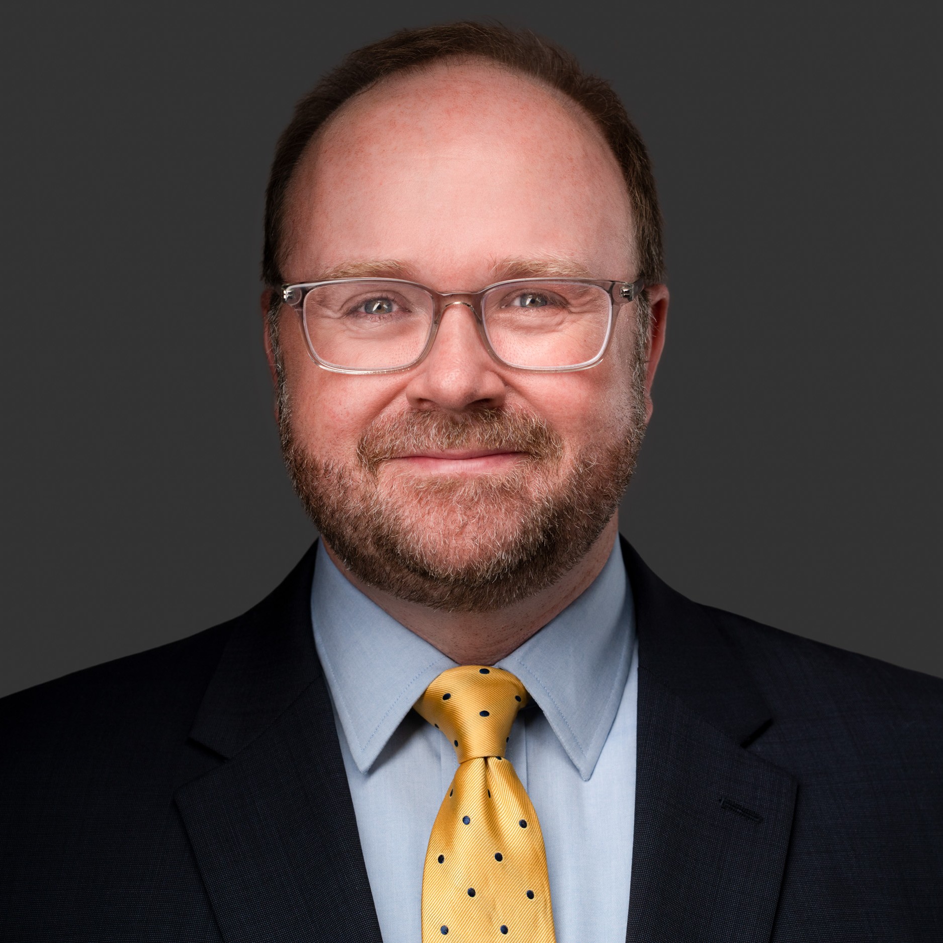 A headshot of DJ Hampton in a suit and yellow tie smiling.