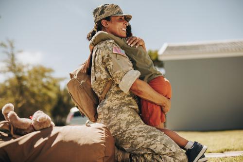 Photo of woman in army fatigues hugging a boy. She's smining.