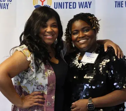 Sonia Hanson and Ruhamah Grooms pose for the camera in front of a Trident United Way step and repeat