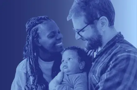 A mother and father holding their child, smiling at the baby.
