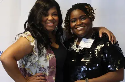 Sonia Hanson and Ruhamah Grooms pose for the camera in front of a Trident United Way step and repeat