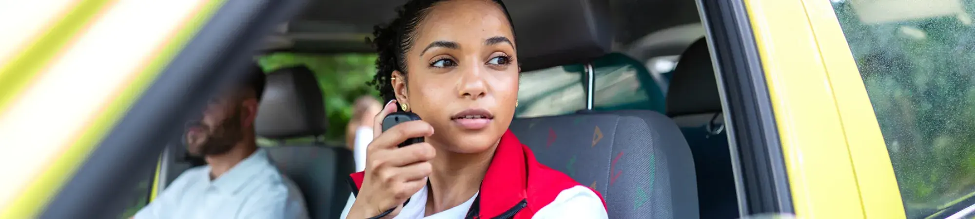 Photo of an emergency responder wearing a red vest in a truck, she holds a CB radio controller and is looking out the window.