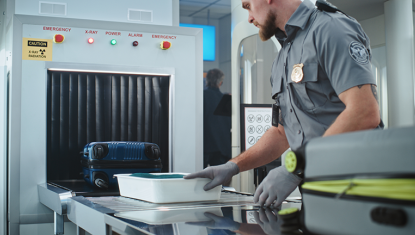 A TSA Agent moves bags beneath a security scanner.