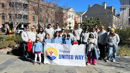 A group of TUW staff stand behind a Trident United Way banner
