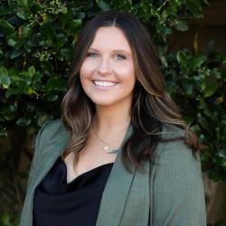 Photo of Chloe standing outside. She has shoulder length brown hair and is wearing a black top and green jacket.