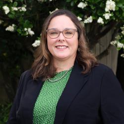 Headshot photo of Christy Boudolf. She is wearing a green top with a black blazer. She has light brown shoulder length hair and is wearing glasses, smiling at the camera