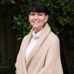 Photo of Helen. She has dark brown hair, is wearing a beige sweater and wrap and is smiling at the camera