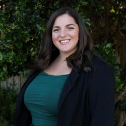 Photo of Lauryn, she has dark shoulder length hair and is wearing a green shirt and black blazer