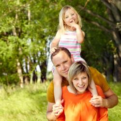 Photo of a child and parents playing outdoors in warm weather. They are posing for the camera.