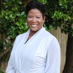 Brittany is standing outside wearing a light colored top, smiling at the camera